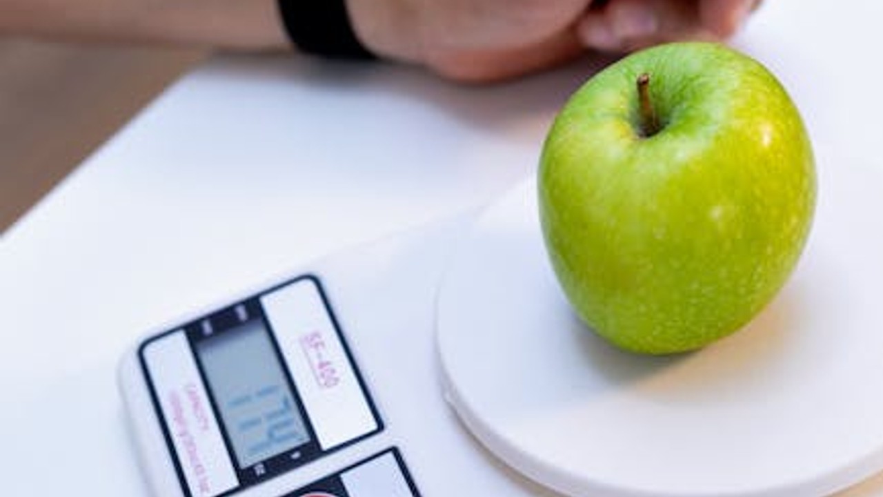 A person weighing food on a scale, symbolizing healthy eating for weight loss.