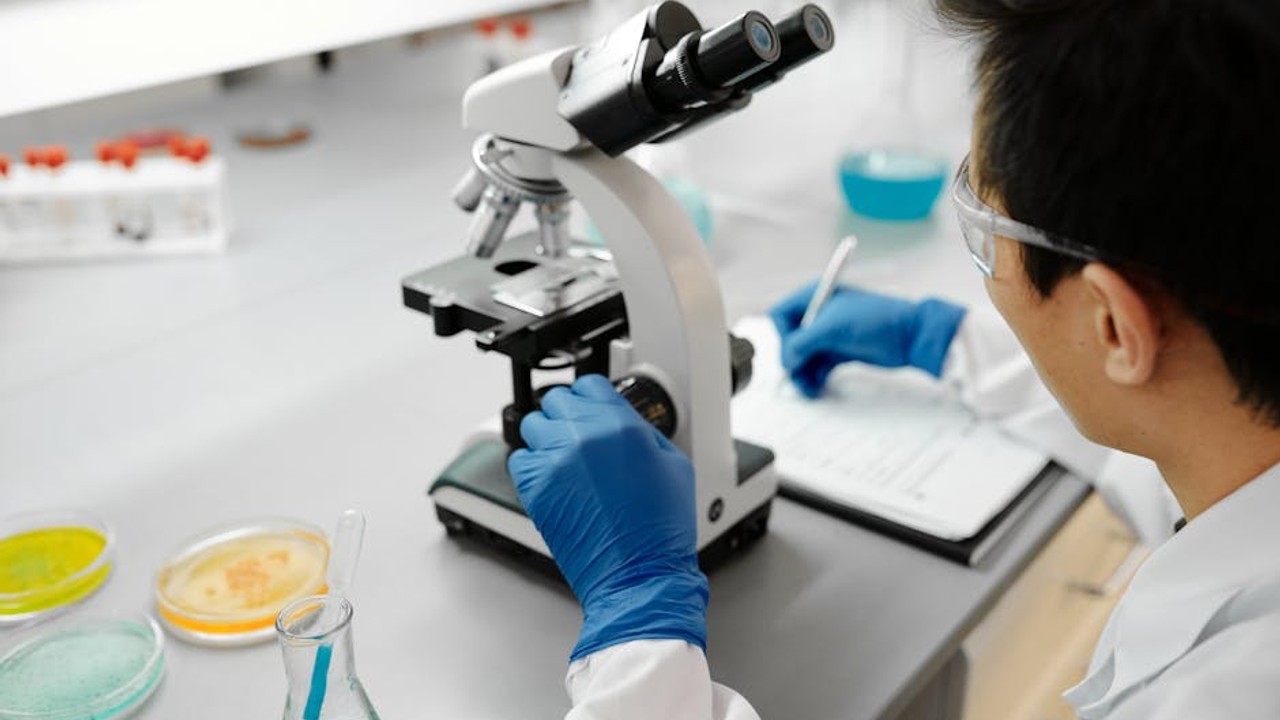A scientist in a lab coat examining a petri dish under a microscope, representing scientific research in skincare